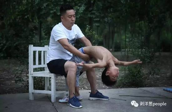 刘甫正在帮助一位小男孩儿练习下腰。刘甫 39岁，13岁开始学杂技 ，2014年收留30多名家境贫困的孩子，免费教练杂技。